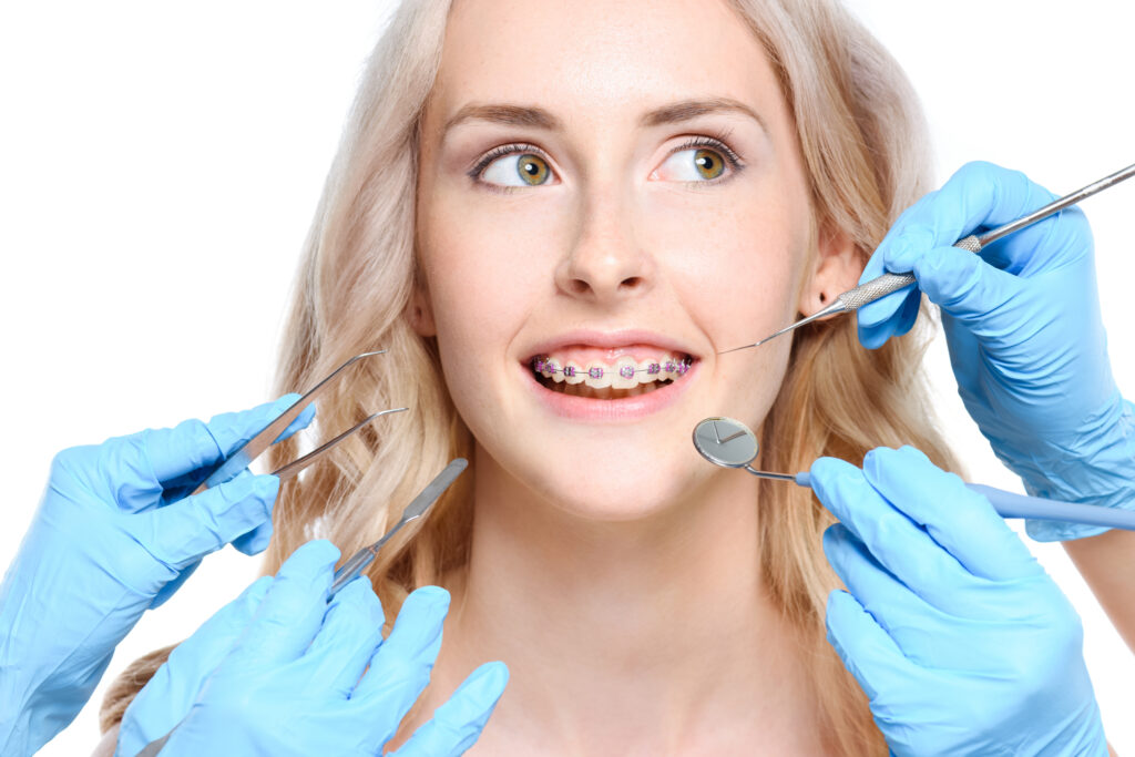 Portrait of a smiling woman with braces with hands holding dentist tools near her face.